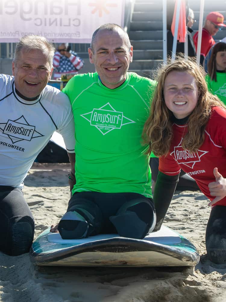 inspirational amputee and two volunteers smiling in wet suits at surf competition.