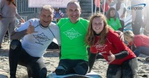 inspirational amputee and two volunteers smiling in wet suits at surf competition.