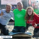 inspirational amputee and two volunteers smiling in wet suits at surf competition.