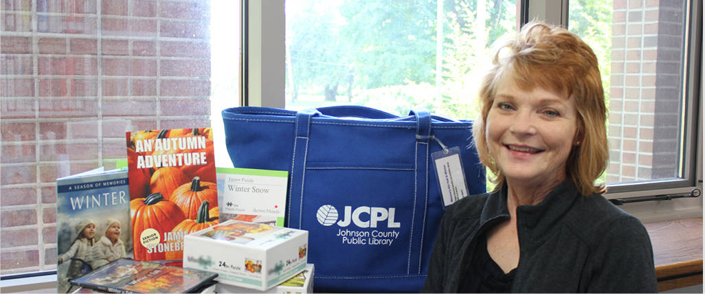 Librarian smiling next to tote bag, books and other materials.