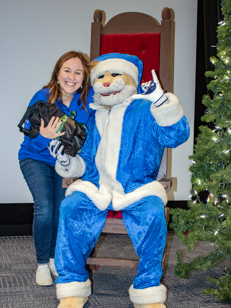 employee holding team holiday gift and posing with company mascot