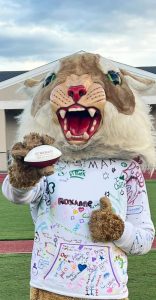 Team mascot holding foam football branded with company information on it.