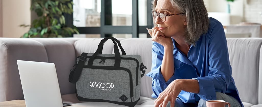 A woman working on a laptop next to a branded messenger bag