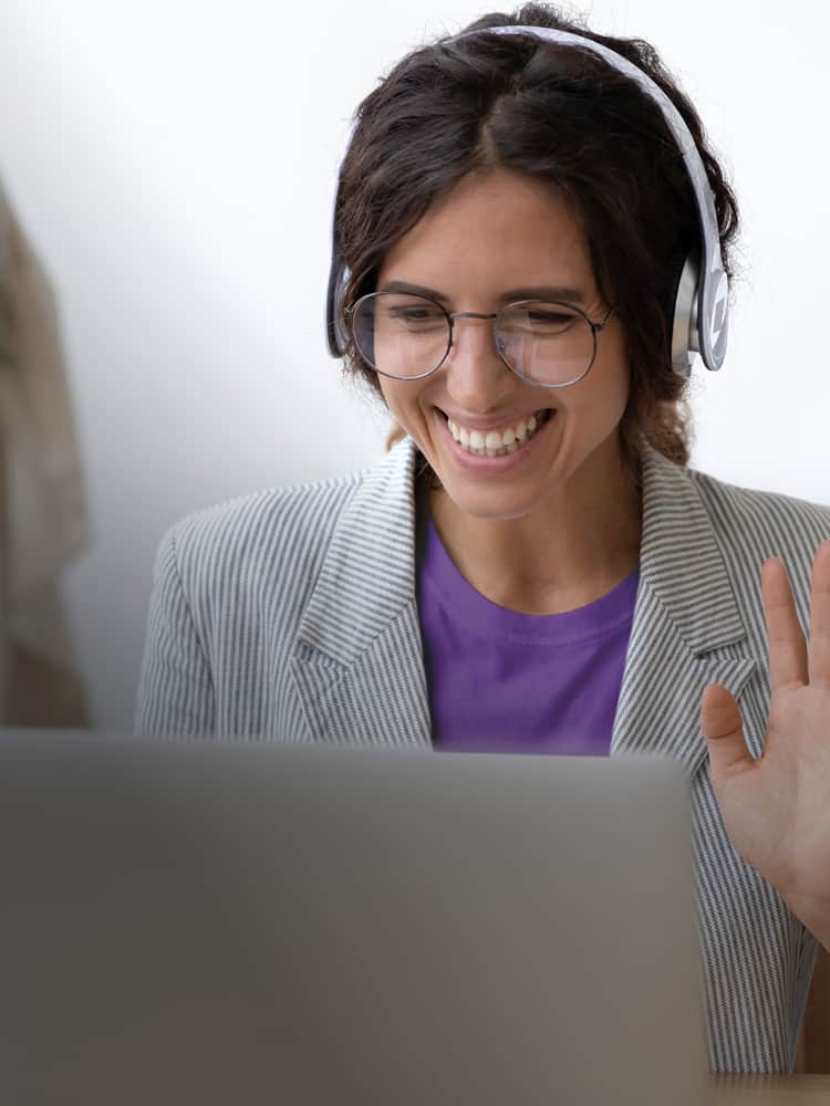 A woman in headphones waves at a computer screen.