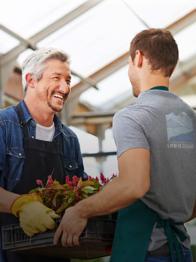 Two colleagues working together in a greenhouse. One is wearing a logoed shirt.