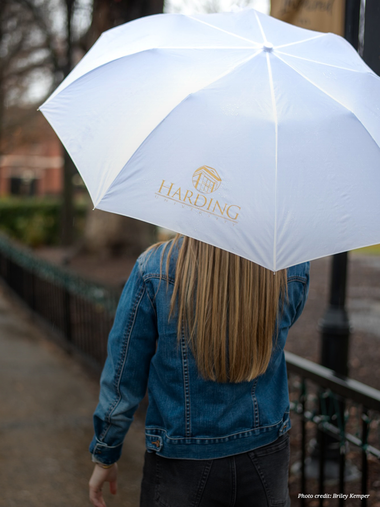 Person walking with branded Harding University umbrella