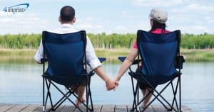 couple holding hands while sitting in bag chairs while looking at lake