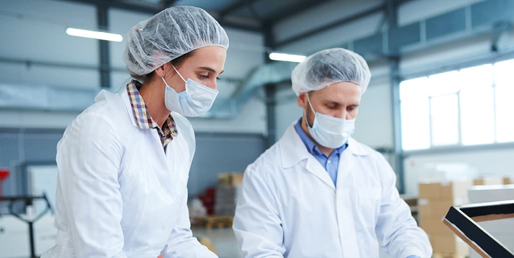 two food workers wearing hair nets and face masks in factory