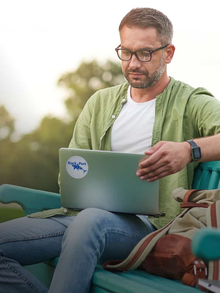 Man on park bench holding laptop with branded sticker