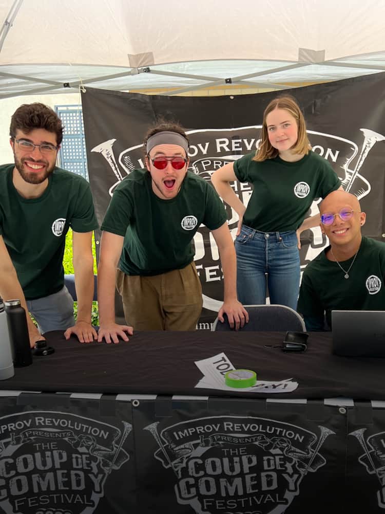 Members of an improv comedy group working a booth to sell tote bags for a cause