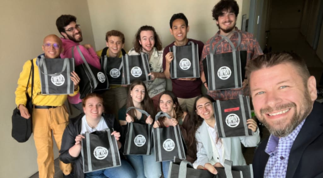 members of Improv Revolution holding up branded tote bags they were selling to raise money.