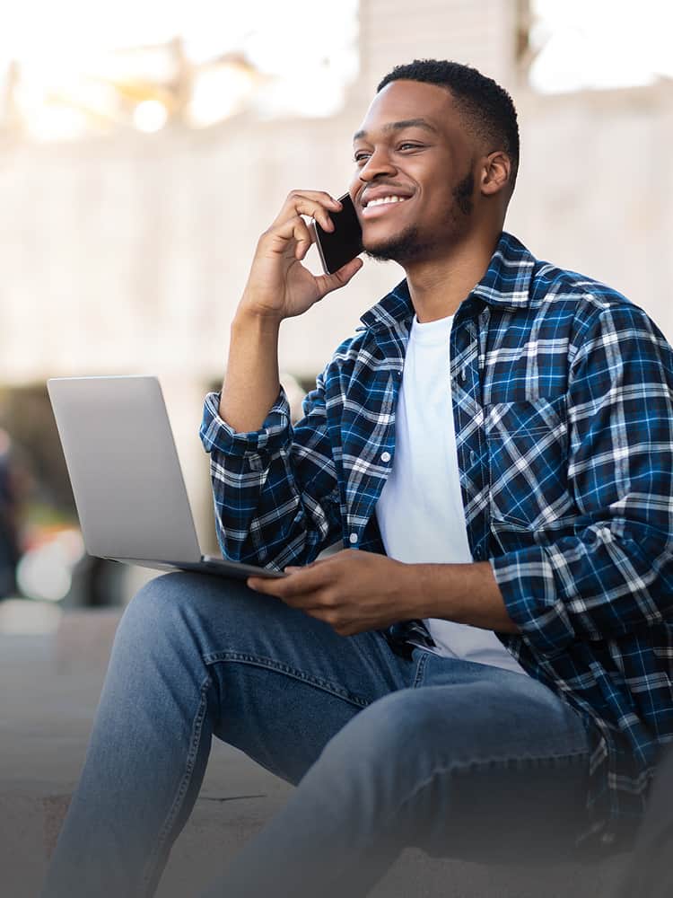 a man on his cell phone sitting with computer on lap