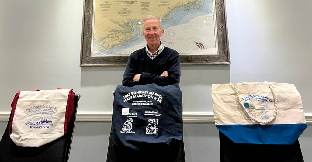 A man poses with various tote bags with logos.