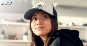 Young woman wearing a hooded sweatshirt and a trucker hat with a logo.