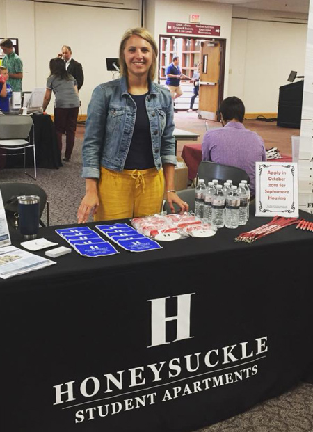 Person standing by table booth promoting Honeysuckle Student Apartments