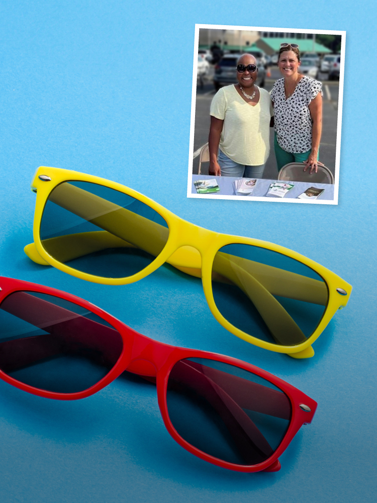People wearing sunglasses at an outdoor display booth with event swag