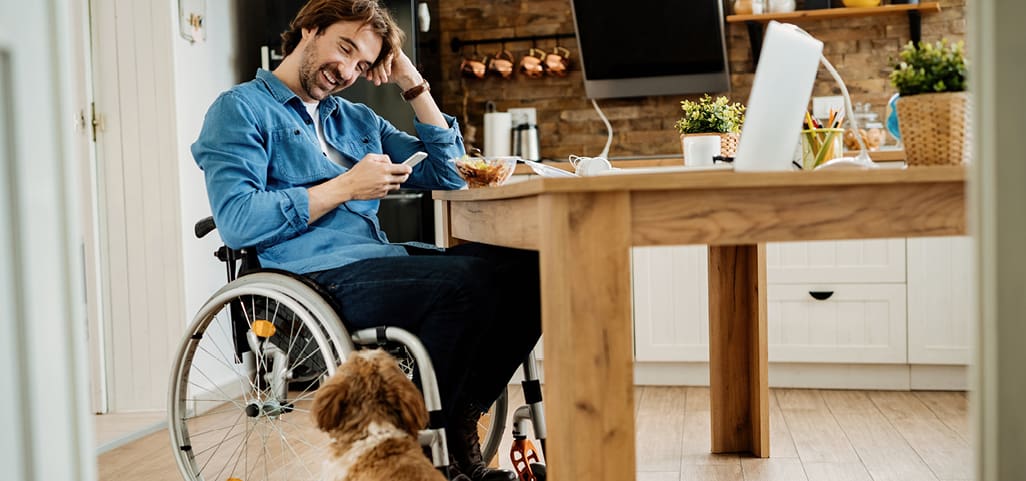 Man in wheelchair at kitchen table looking at cell phone