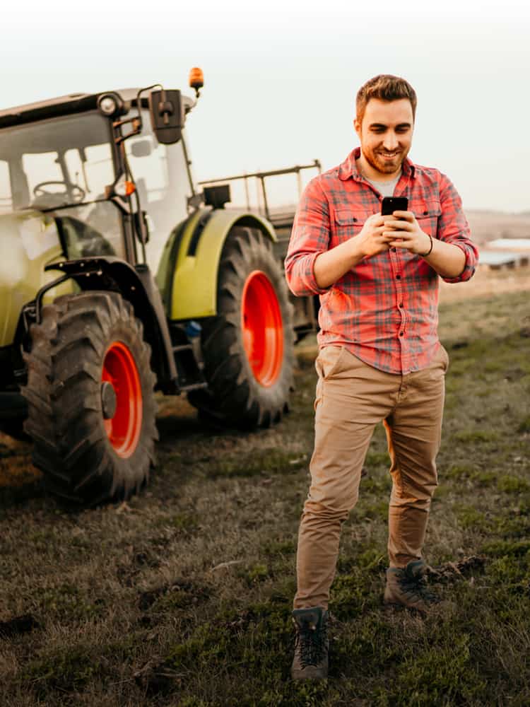 Farmer looking at cell phone with tractor behind him