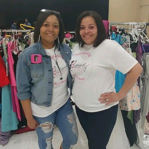 Two volunteers posing in their branded T-shirts, standing in front of clothing racks