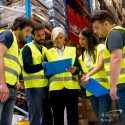 Photo of 5 people in a warehouse wearing safety vests and looking at a set of safety plans. Safety giveaways to reward and promote sound practices