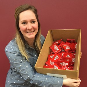 Woman smiling and holding a cardboard box of KitKats in front of a red wall 