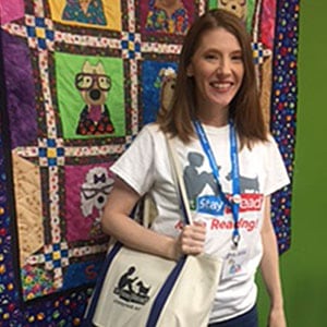 Woman holding canvas bag and smiling in front of a quilt hanging on a green wall