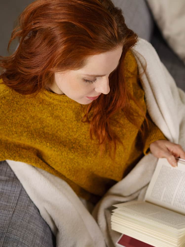 Woman on a couch reading a book with a promotional blanket on her lap