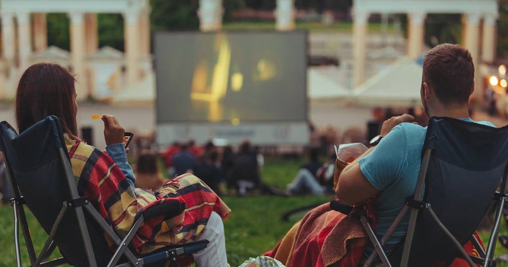 A man and woman sitting on lawn chairs with blankets on their laps while watching an outdoor movie