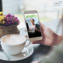 photo of person in coffee shop looking at phone. Screen as the latest issue of amplify digital magazine on it and the cover image talking about how promotional giveaway items are used in interviews.