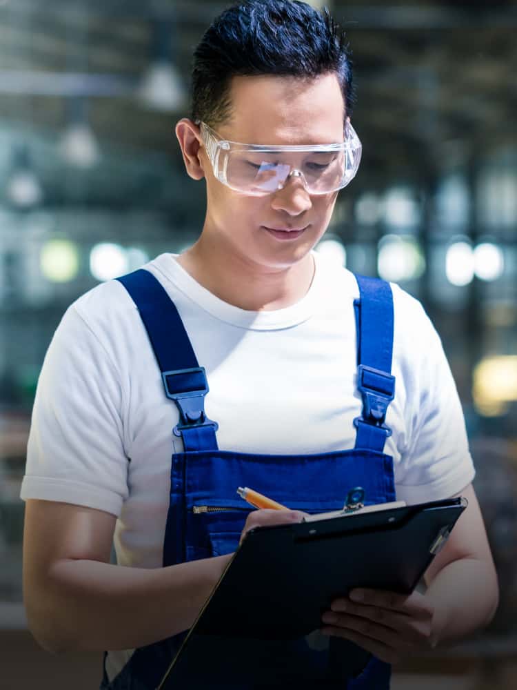 A person wearing safety goggles writing on a clipboard.