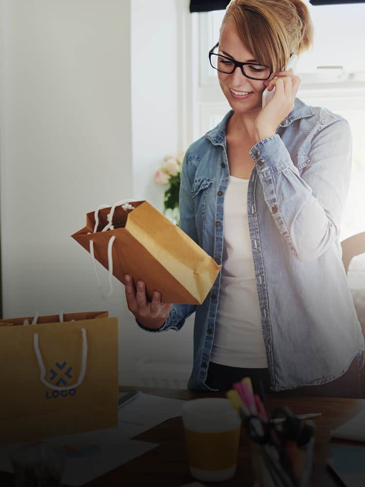 A woman on the phone looking at a logo bag.