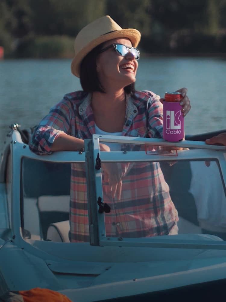 A woman sitting on a boat holding a drink in a promotional can cooler.