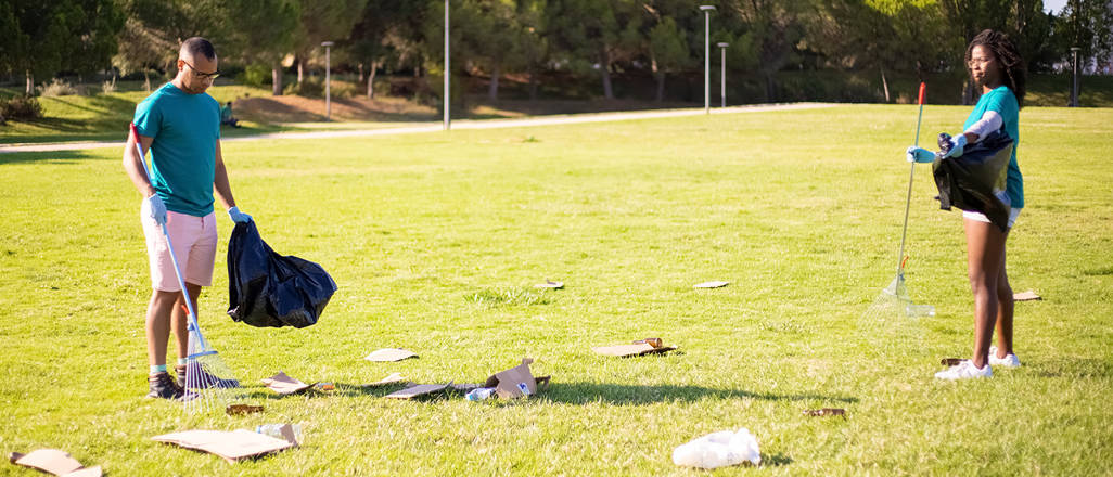 Two volunteers cleaning up trash in a field.