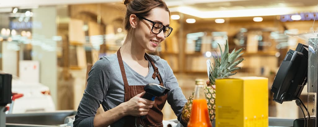 A woman in glasses scanning a pineapple in a store.