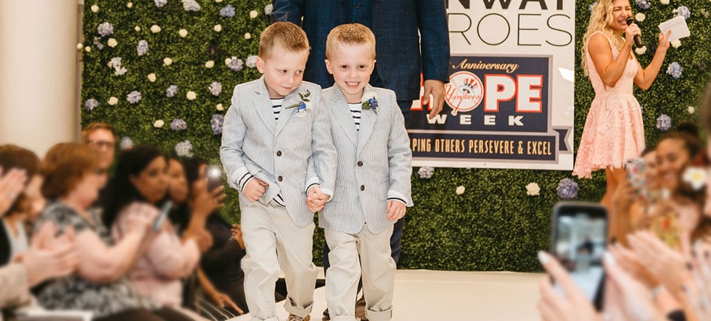 Two young boys walking down a fashion show runway as part of a Runway Heroes event