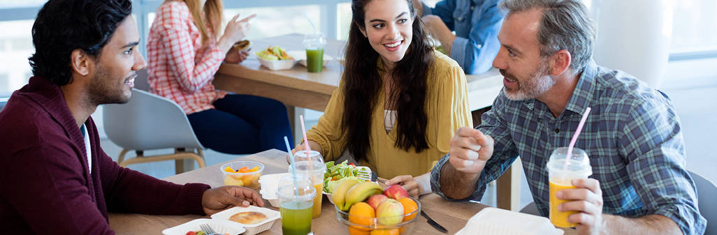 Three employees eating healthy lunch food in work cafeteria area