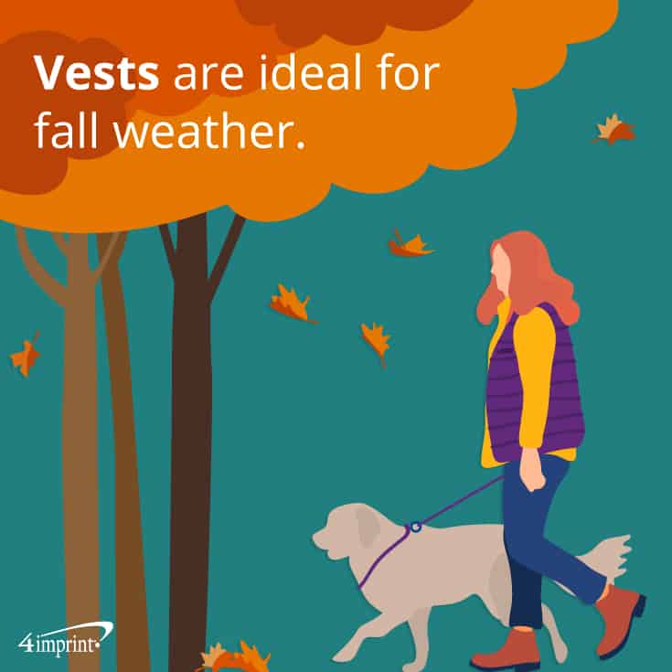 Woman in a vest walking her dog outside next to trees and falling leaves