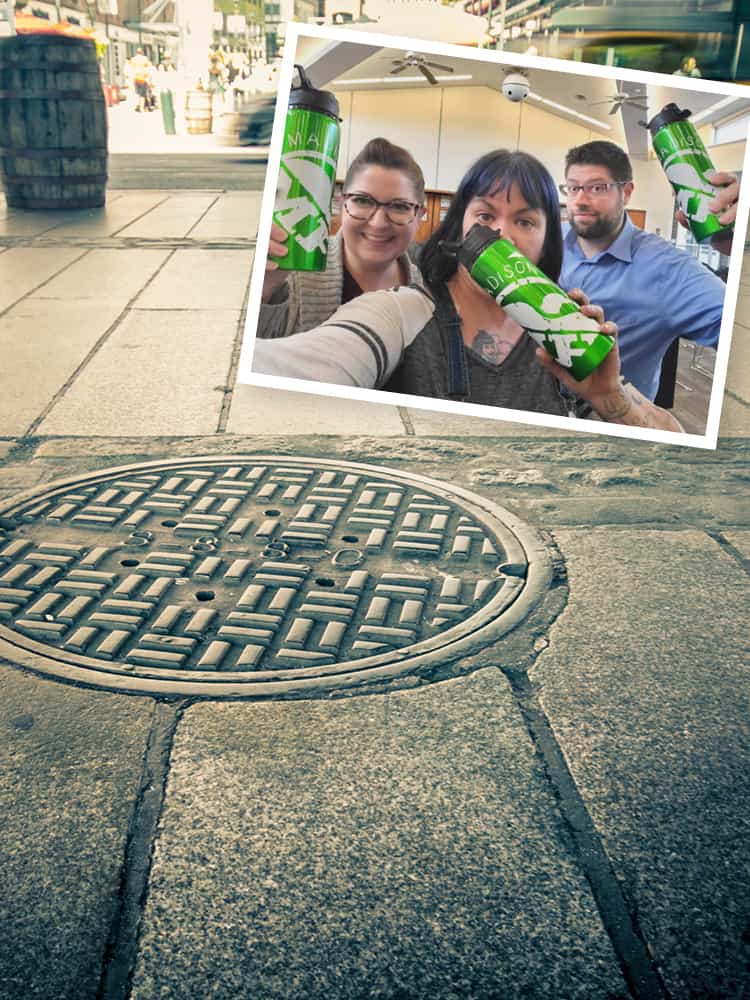 Three artists holding promotional water bottles based on the design of a city man-hole cover