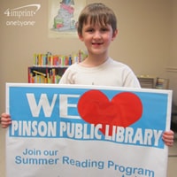 Young boy smiling and holding a library display sign